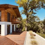 Einfamilienhaus bayerisch, traditionell, mit bodentiefen Fensterelementen. Gehackte Holzschalung mit Tiroler Eckplatt Verbindung.