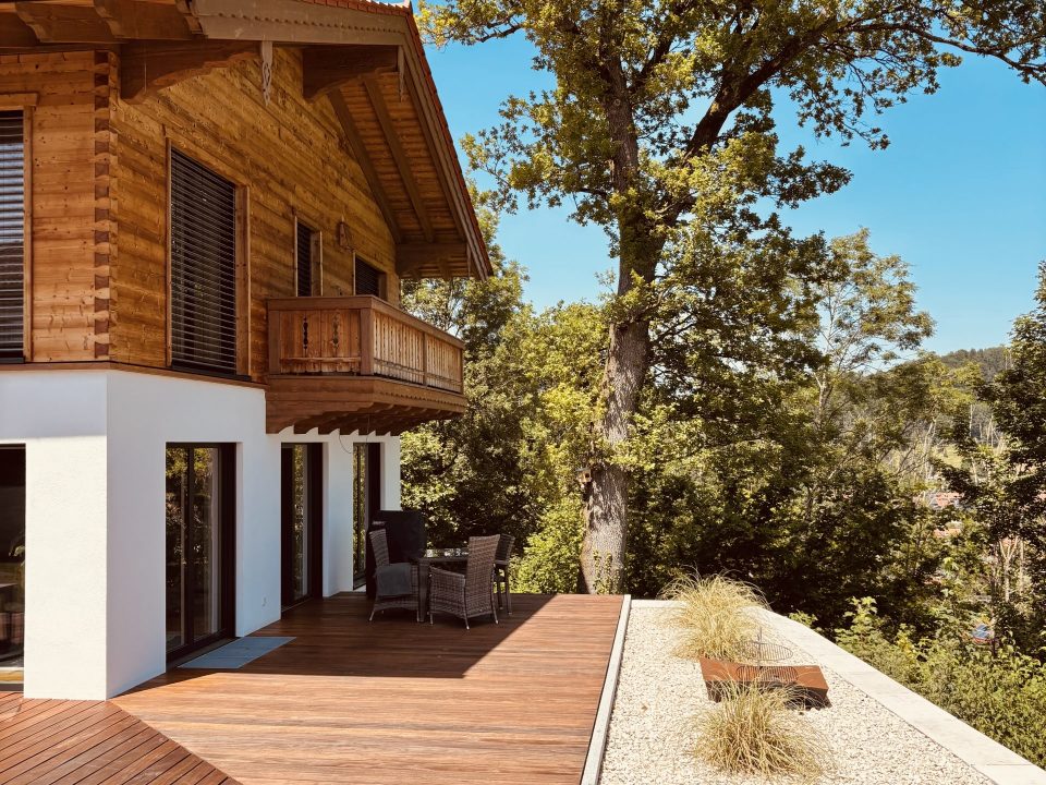 Einfamilienhaus bayerisch, traditionell, mit bodentiefen Fensterelementen. Gehackte Holzschalung mit Tiroler Eckplatt Verbindung.